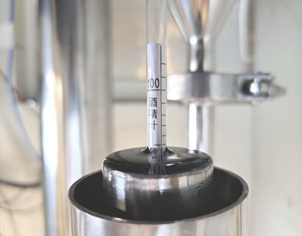 Image of diy distilling taking an alcoholmeter reading from a proofing parot